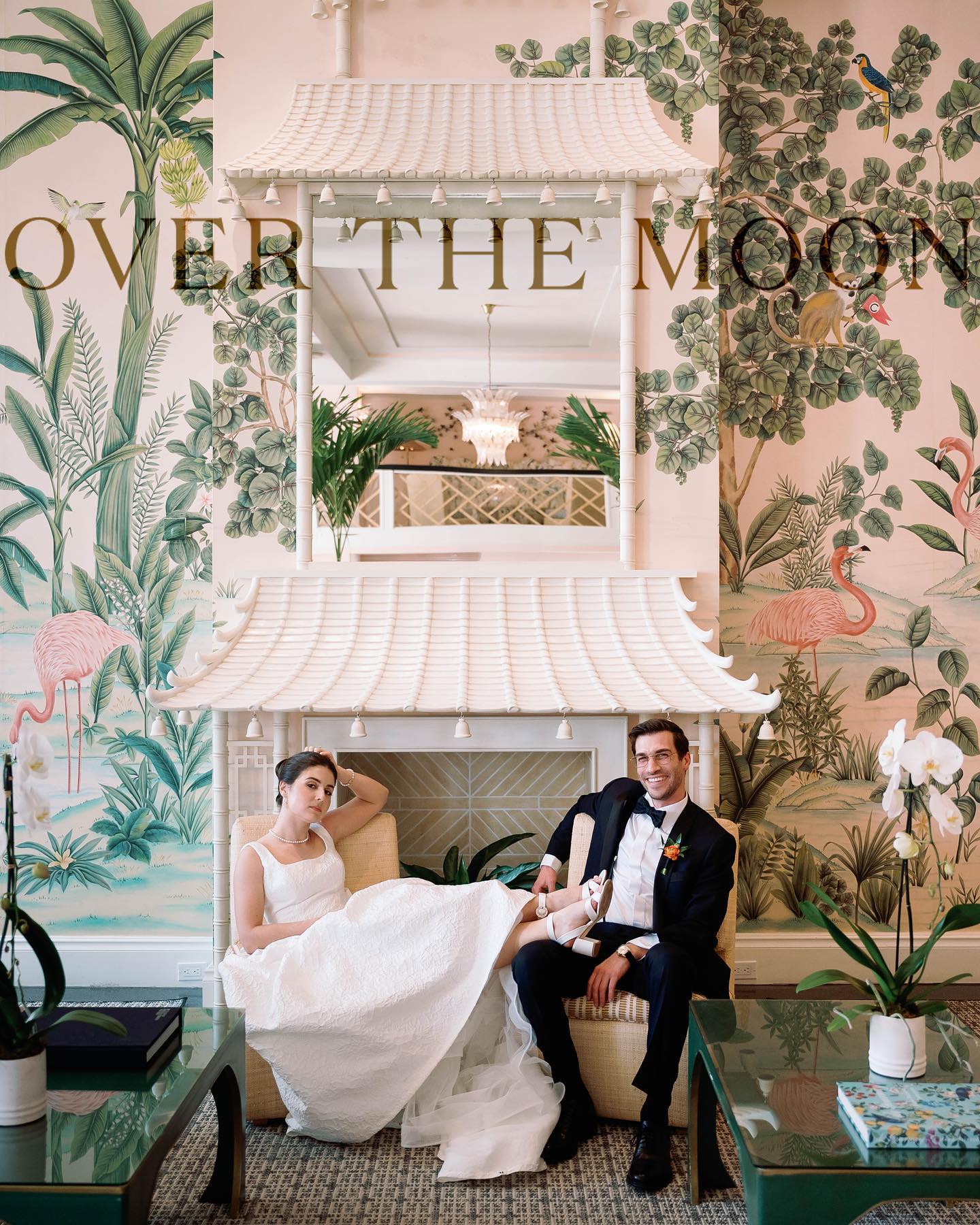 Over the Moon publication feature showing a bride and groom seated across a bench with pink printed wallpaper behind them.
