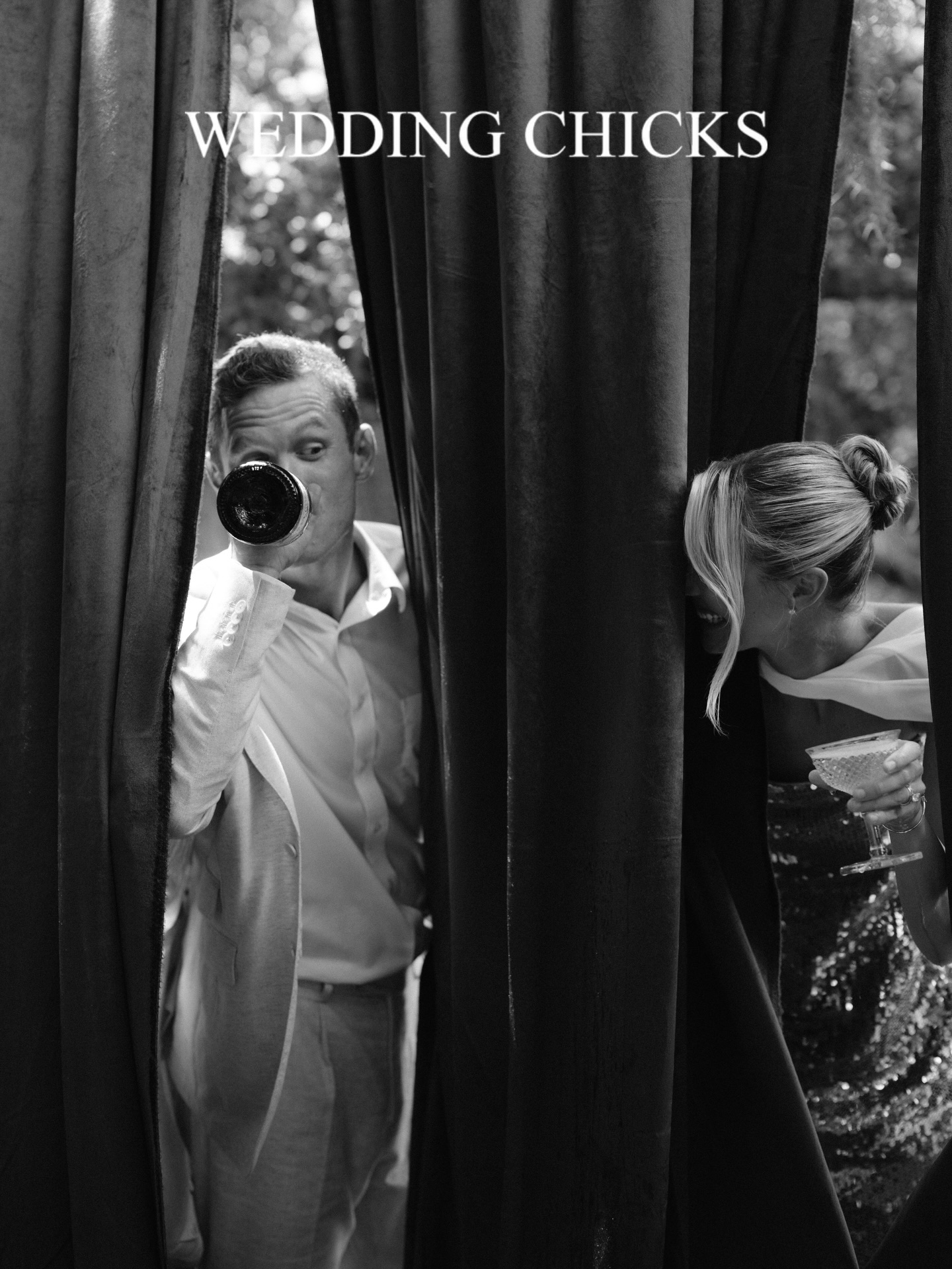 Bride and groom peaking around curtains at each other while the groom drinks from a bottle.